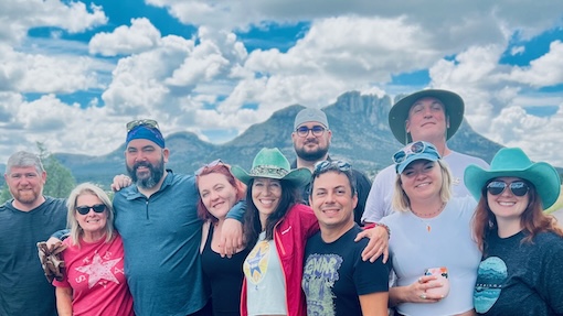 A group of people from WildGins and Favorite Branmds in hats stands together, smiling in front of a scenic Davis Mountains backdrop.